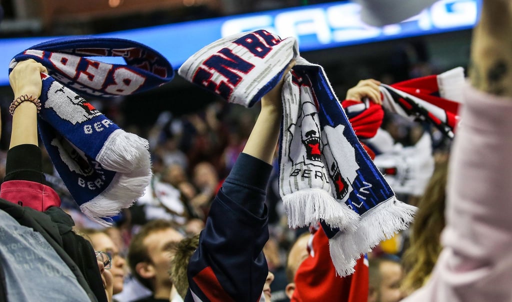 Fans halten jubelnd ihre Schals mit Eisbären Logo in die Luft.