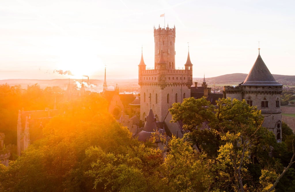 Die aufgehende Sonne taucht die Wälder und Schloss Marienburg am Morgen in warmes Licht.