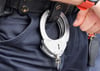 Handfesseln aus Metall hängen am Gürtel eines Polizisten.