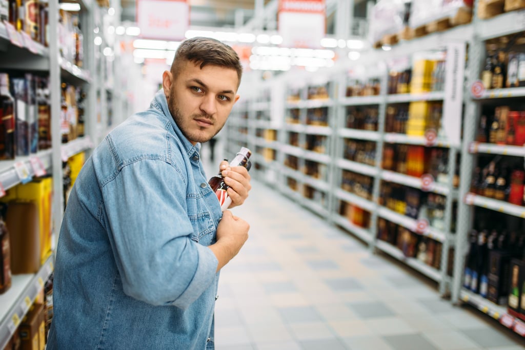 Ein Mann stiehlt eine Flasche aus dem Spirituosenregal eines Lebensmittelmarktes (Symbolbild).