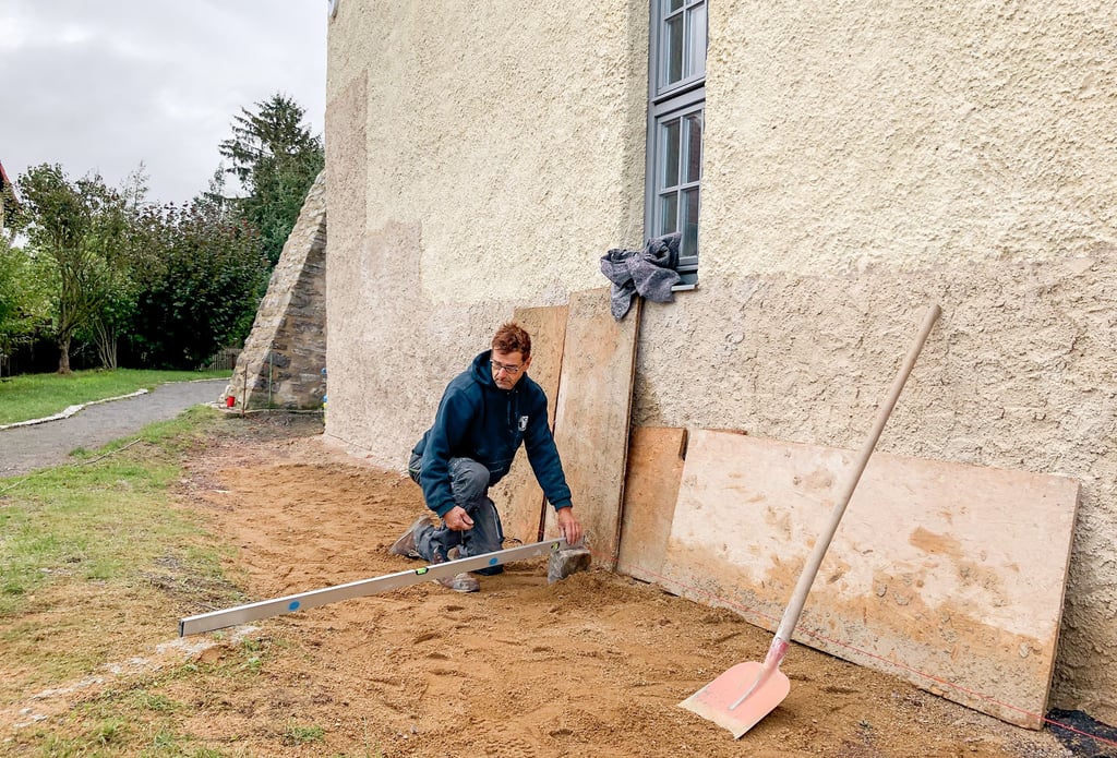 Das Mauerwerk im Sockelbereich ist repariert, nun wird ein Traufstreifen angelegt. Steinmetz Thomas Laue legt dafür die Wasserwaage an.