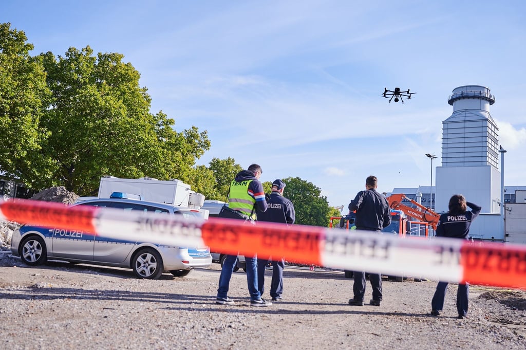 Polizisten stehen hinter einer Absperrung auf der Baustelle in Berlin-Moabit, wo eine Weltkriegsbombe gefunden wurde und bedienen eine Drohne.