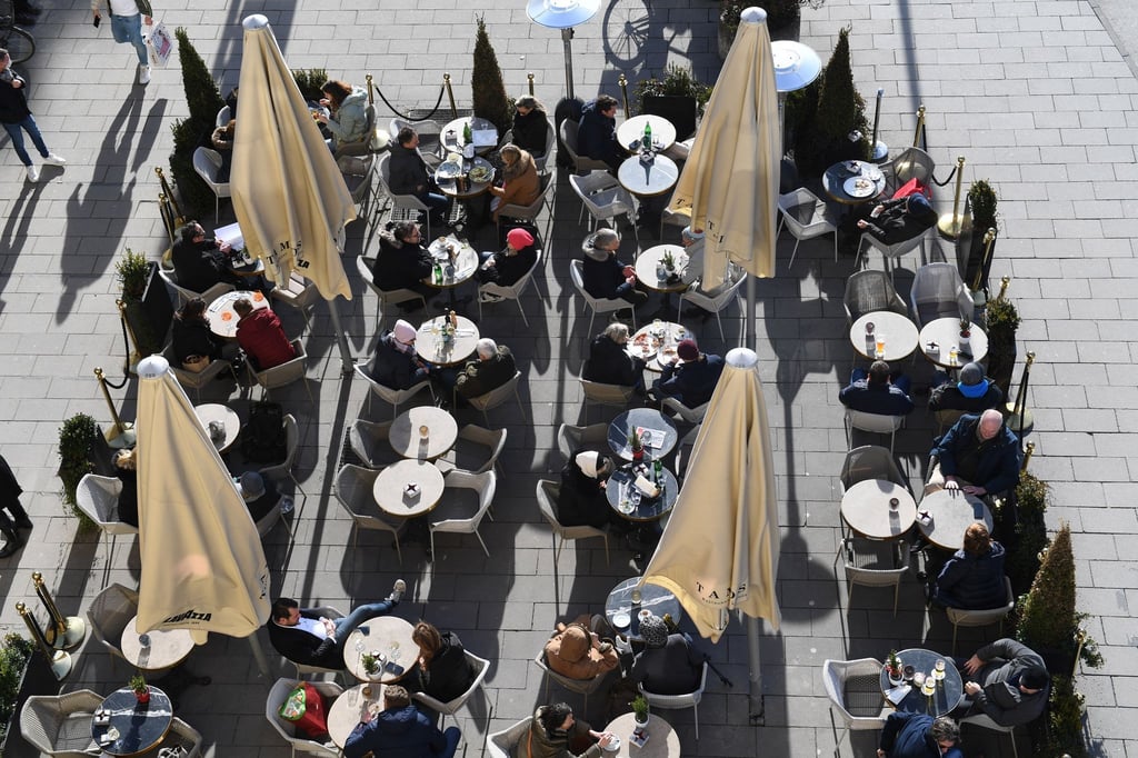 Gäste sitzen vor einem Café in der Sonne.