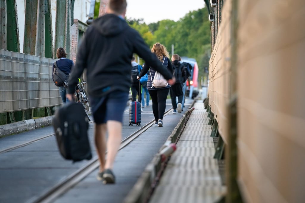 Fahrgäste laufen mit Koffern und anderem Gepäck über die Schleibrücke bei Lindaunis.