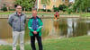 Tischlermeister Erik Müller und Jürgen Wiesener, Vorsitzender Angelfreunde Lützen, stehen am Dorfteich in Meuchen. Hinter ihnen schwimmt das neue Entenhaus.