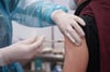 Ein Mitarbeiter eines Impfzentrums impft einen Mann gegen Corona.