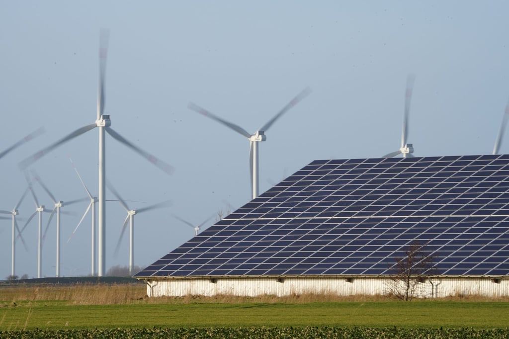 Windenergieanlagen stehen neben einer Halle mit Photovoltaik-Anlagen.