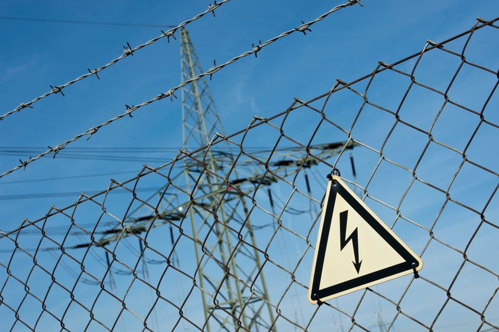 Ein Gefahrenschild für Elektrizität ist vor einer Stromtrasse zu sehen.