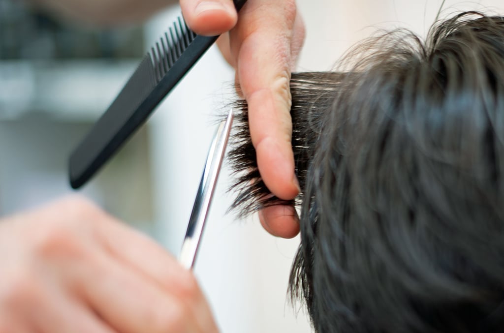Ein Friseur schneidet in einem Salon einer Kundin mit der Schere die Haare.