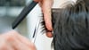  Ein Friseur schneidet in einem Salon einer Kundin mit der Schere die Haare.