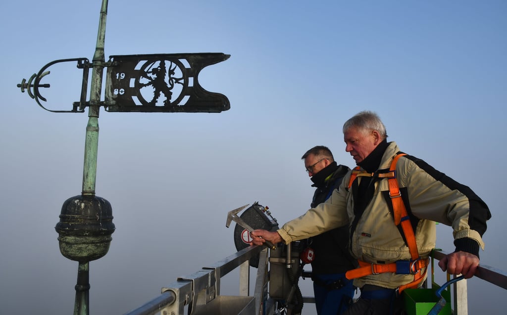 Dachdecker Helmut Kempe (vorn) aus Hillersleben schwingt sein Werkzeug, um die Schifferplatten am Kirchturm zu erneuern. An seiner Seite steht René König , der die Arbeitsbühne bedient.