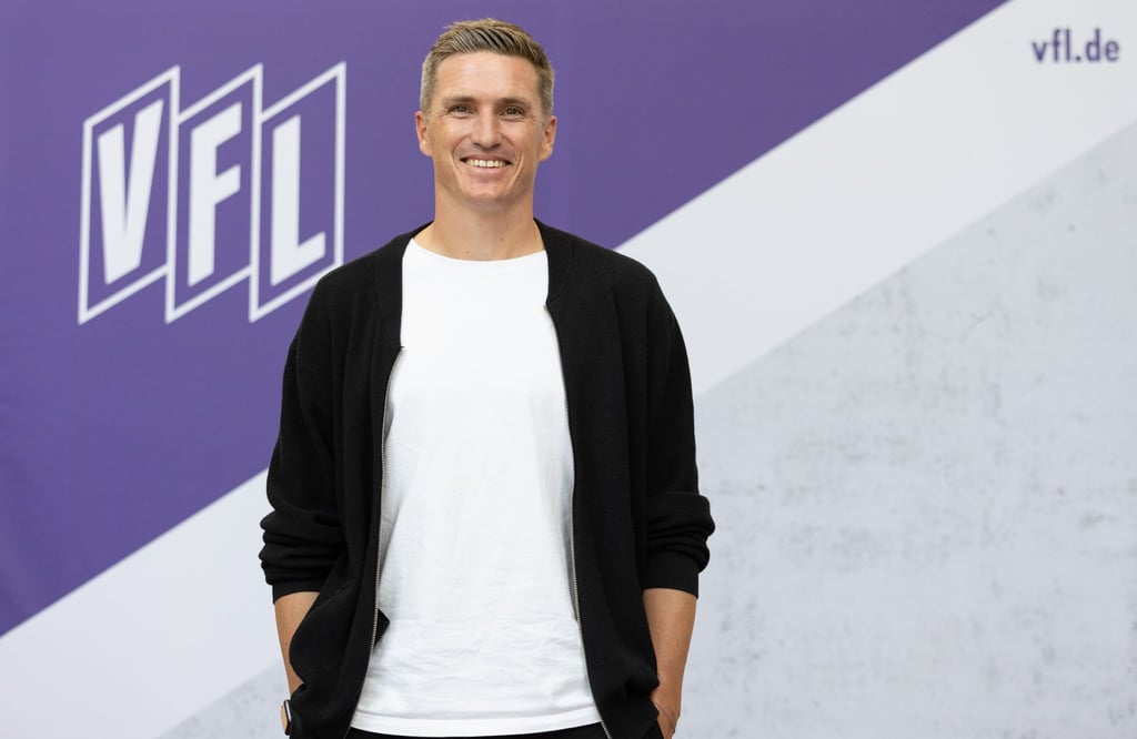 Trainer Tobias Schweinsteiger posiert vor einem Vereinslogo im Stadion an der Bremer Brücke.