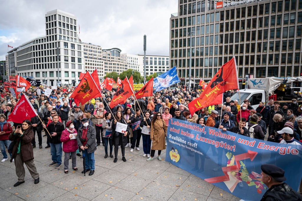 Teilnehmer stehen auf der Demonstration „Heizung, Brot & Frieden! Protestieren statt frieren“ am Potsdamer Platz mit Fahnen und Plakaten.
