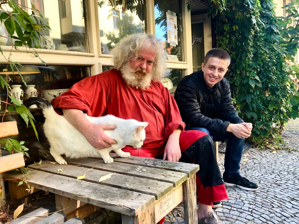 Töpfer René Kloth (links) und Katze Lutz bekommen in der Paulustöpferei in der Hardenbergstraße acht täglich Besuch von Nachbarn wie Asad Rujovic. Da der Transporter des Keramikers einen Motorschaden hat, sammeln die Hausbewohner nun Spenden.