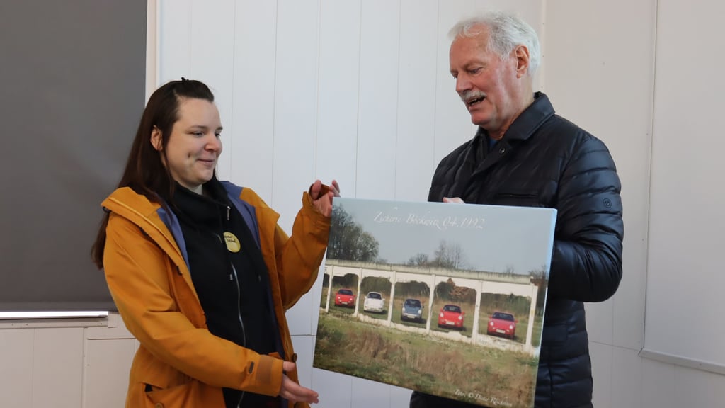 Porsche-Testfahrer Dieter Röscheisen überreicht Verena Treichel eine Fotografie mit Porsches in der offenen Mauer.