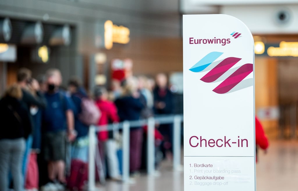 Reisende stehen am Flughafen am Check-in-Schalter der Fluggesellschaft Eurowings.