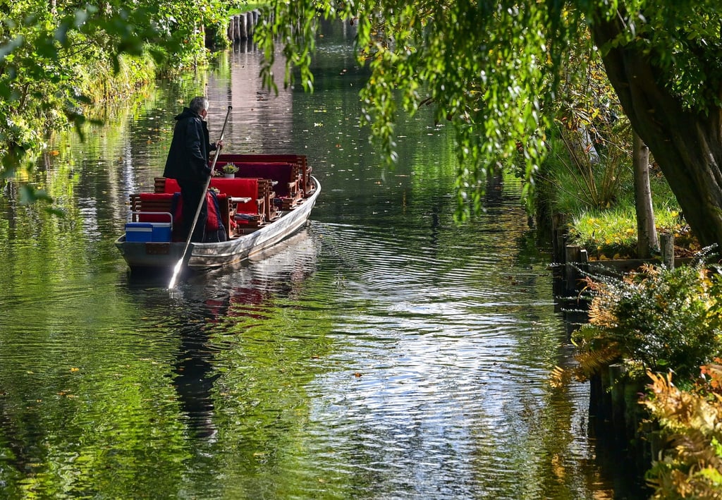 Ein Fährmann stößt mit seinem Kahn auf einem Fließ im herbstlichen Spreewald.