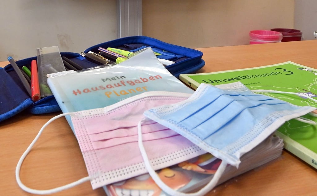 Masken liegen in einem Klassenzimmer auf einem Schulbuch.