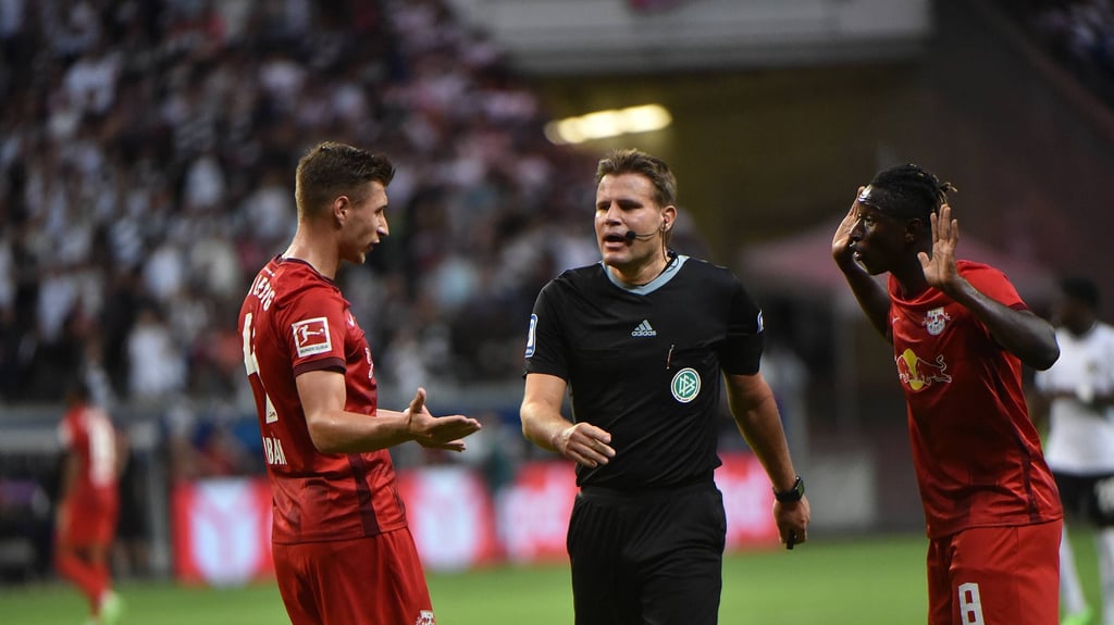 Felix Brych diskutiert mit Willi Orban (l.) und Amadou Haidara (r.).