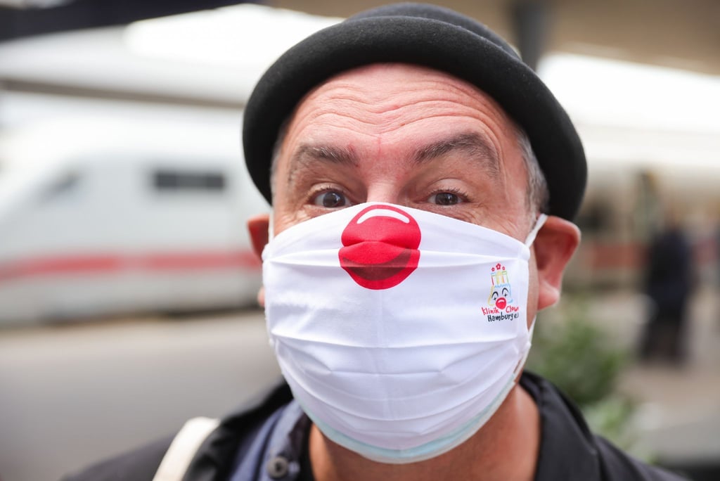 Ein Klinikclown trägt seine rote Nase auf seiner Schutzmaske.
