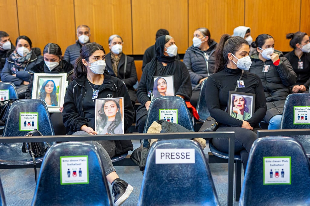 Angehörige der Getöteten sitzen mit Porträtfotos der getöteten Frau beim Prozessauftakt in einem Saal vom Landgericht Hildesheim.