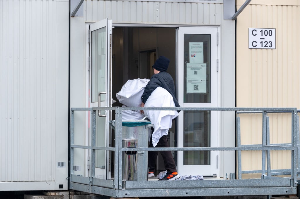 Ein Mann geht mit Bettzeug in einen Container mit Wohnbereichen in einer Aufnahmeeinrichtung.