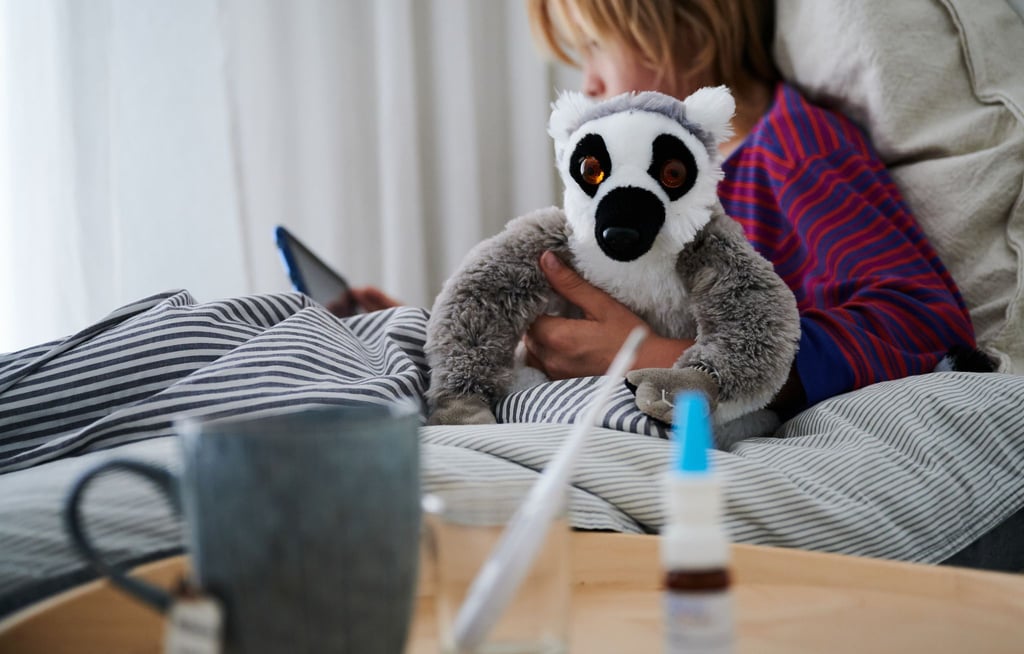 Nasenspray und eine Tasse Tee stehen vor einem Bett, in dem ein krankes Kind sitzt.