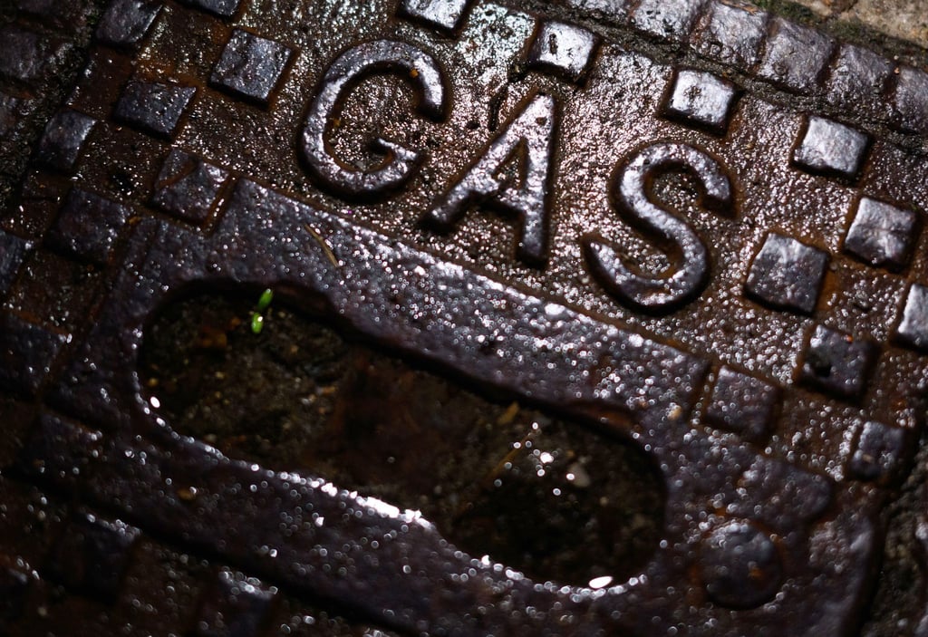 Ein Schriftzug „Gas“ steht in einem Wohngebiet auf einer gusseisernen Straßenkappe.