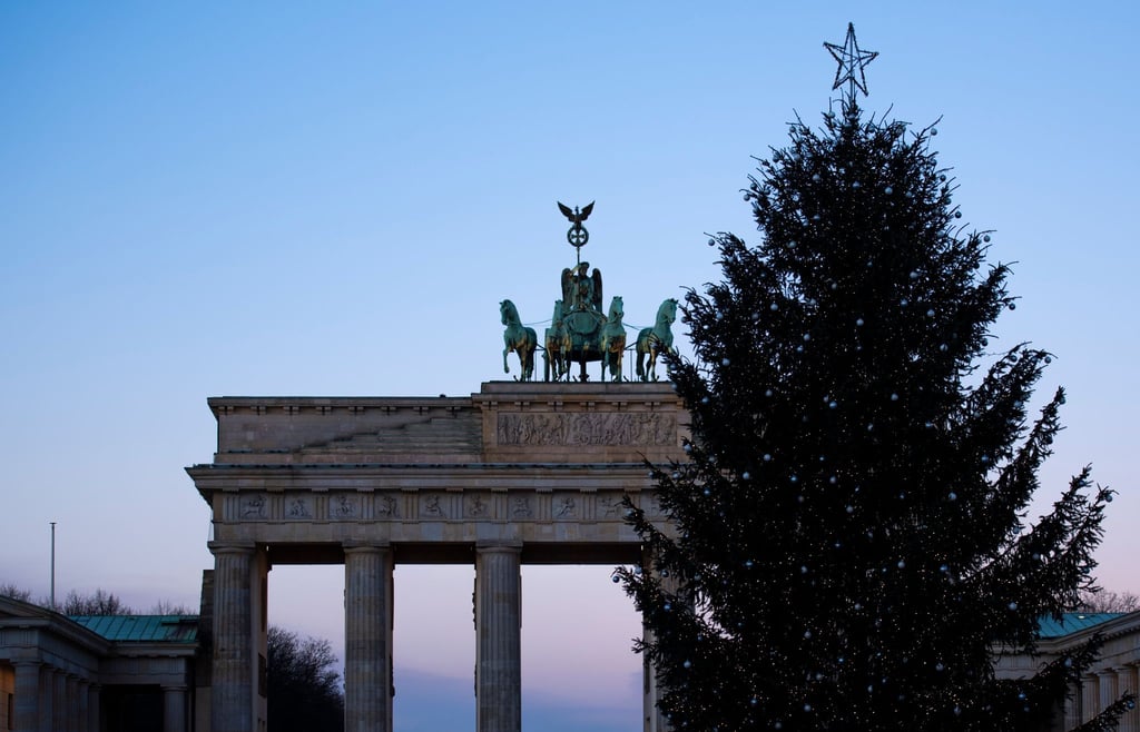 Hinter einem geschmückten Weihnachtsbaum steht das Brandenburger Tor.