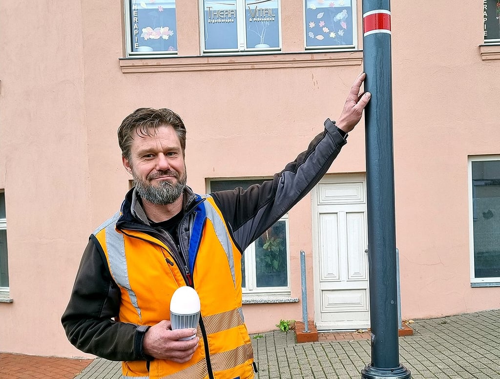 Stadtelektriker Ralf Westphal zeigt in seiner rechten Hand eine LED-Leuchte und die rot-weiße Reflektorfolie an einem Lampenmast in der Havelberger Bahnhofstraße.