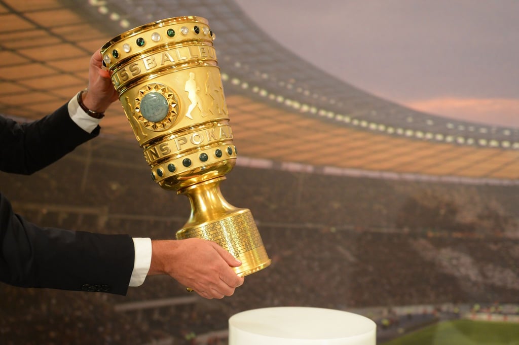 Ein Mann nimmt den DFB-Pokal von seinem Sockel.