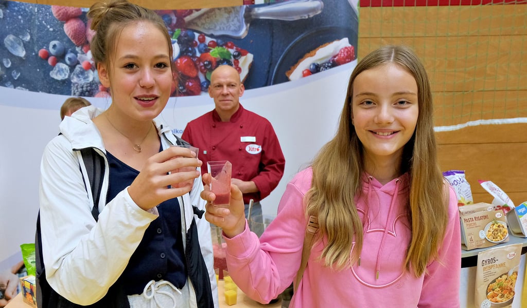 Lina Jahn (l.) und Pia Tittel stoßen bei der Jobbörse in der Jessener Mehrzweckhalle mit Saft an und informieren sich über Ausbildungsplätze.