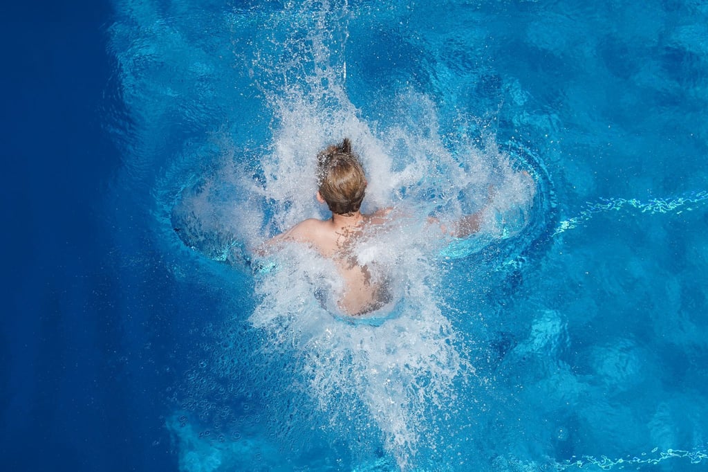 Ein Junge springt in einem Freibad ins Wasser.