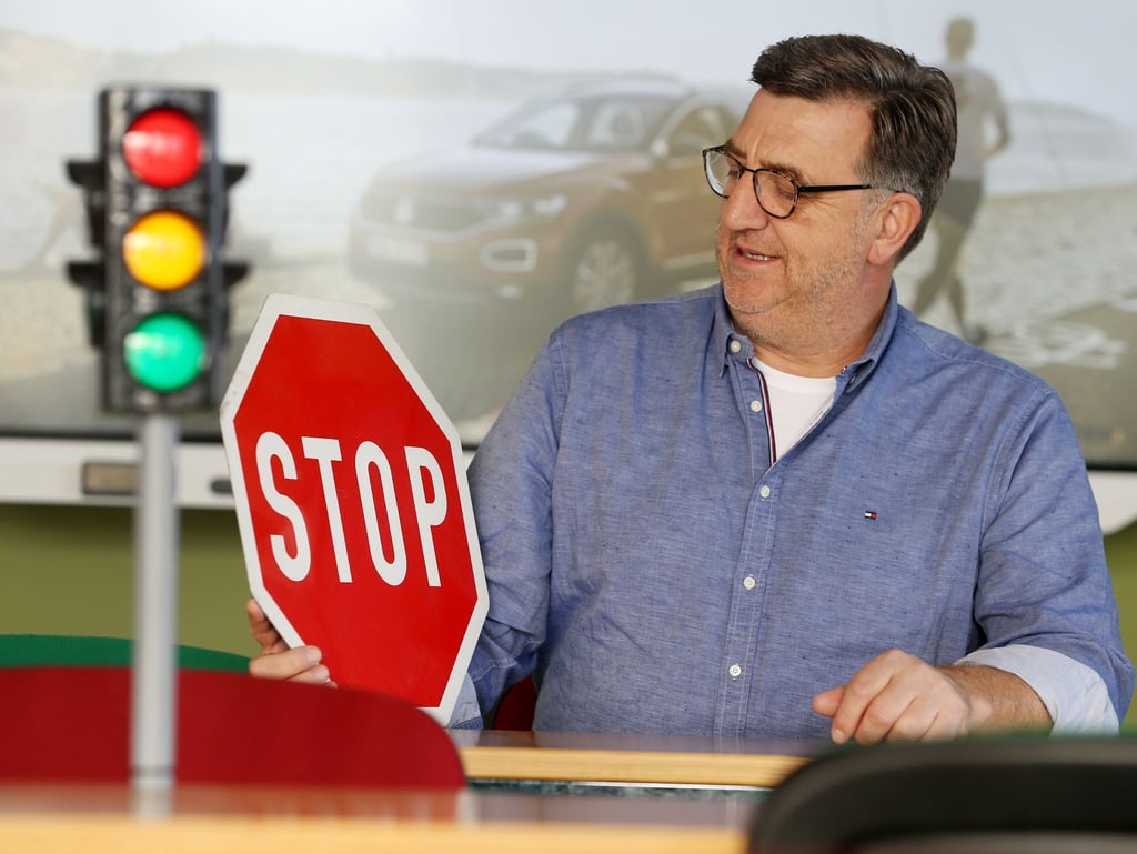 Fahrlehrer Horst Wintgen sitzt mit Ampel und Verkehrsschild im Übungsraum seiner Fahrschule.