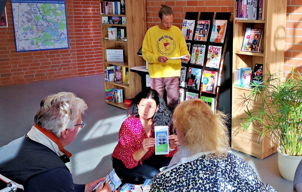 Jutta Zacharias-Lange erläutert einem Ehepaar aus Niedersachsen hiesige Angebote, Bibliotheksmitarbeiter Ray Günther ordnet das Angebot im Zeitschriftenregal.