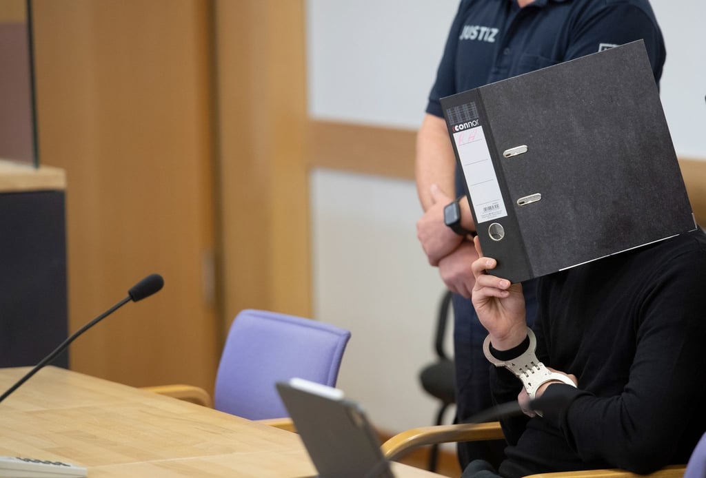 Der Angeklagte hält sich in einem Saal des Landgerichts Neuruppin einen Ordner vor das Gesicht.