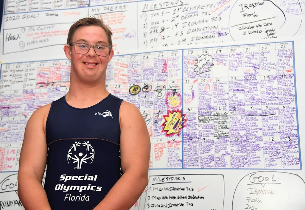 Triathlet Chris Nikic steht in seinem Zimmer vor einer Tafel, auf der er seine Traingseinheiten notiert hat.