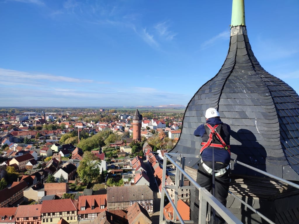 Mit der Stadt als Panorama ist Dachdecker Johannes Vogt am Nordturm der Kirche "Unser Lieben Frauen" in Burg mit der Reparatur des Schieferdaches beschäftigt.