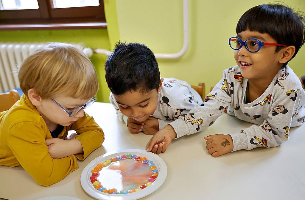 Die Kinder der Kita „Bussi Bär“ erzeugen bei einem Regenbogen-Experiment mit Smarties ein buntes Farbenspiel.