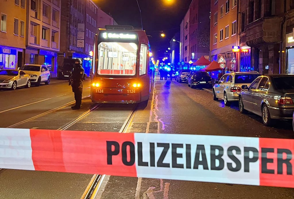 Ein Polizist steht mit einer Maschinenpistole hinter einer Polizeiabsperrung.