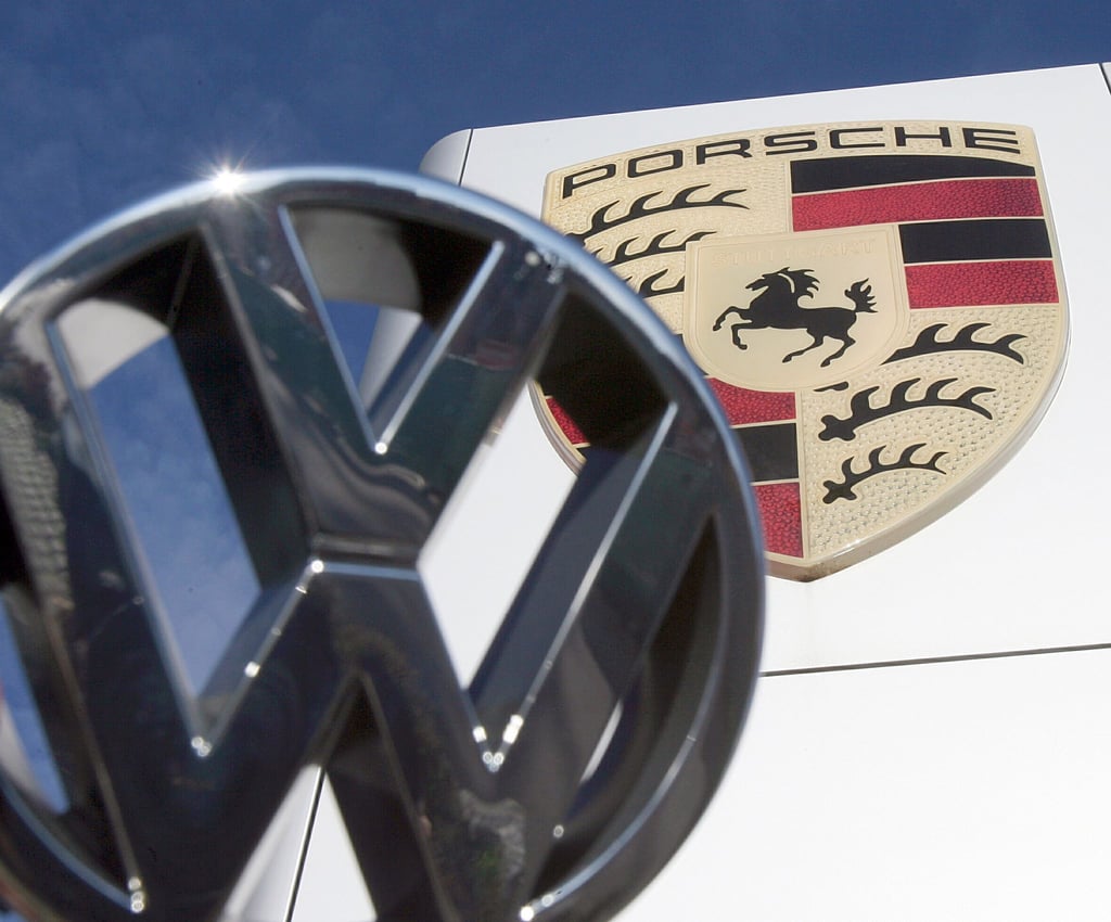 Ein VW-Logo ist vor einem Porsche-Firmenlogo vor einem Porsche-Center zu sehen.