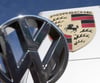 Ein VW-Logo ist vor einem Porsche-Firmenlogo vor einem Porsche-Center zu sehen.