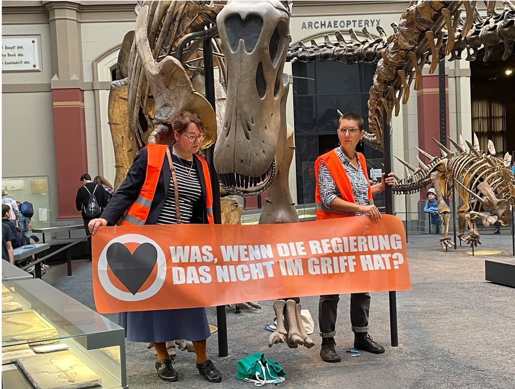 Zwei Klimaaktivistinnen mit einem Banner haben sich im Berliner Museum für Naturkunde an den Haltestangen eines Dinosauriers festgeklebt.