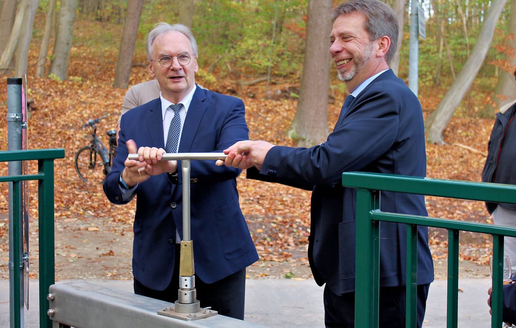 Reiner Haseloff (links) und Denis Loeffke betätigen manuell den Regler, mit dem der Wasserablauf am neuen Verteilerbauwerk des Suenbachs in Ilsenburg künftig koordiniert werden kann.