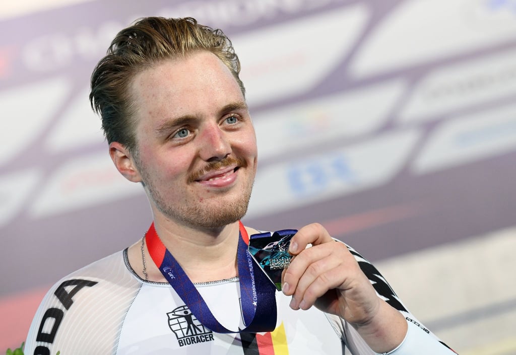 Moritz Malcharek zeigt auf dem Podium eine Medaille.