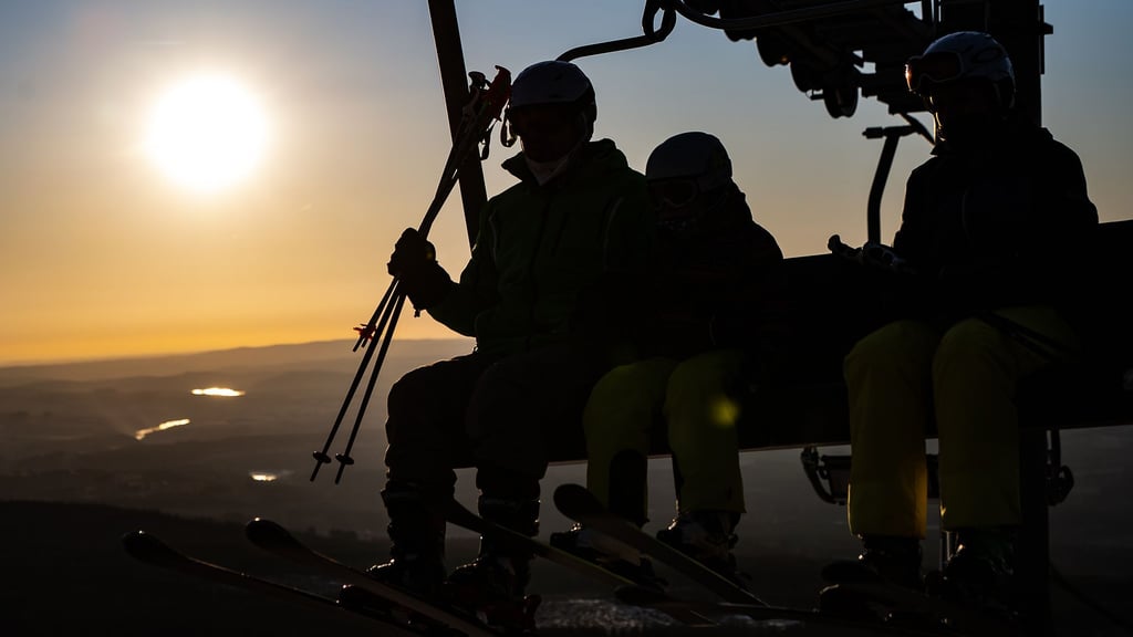 Wintersportler sitzen bei Sonnenaufgang im Sessellift.