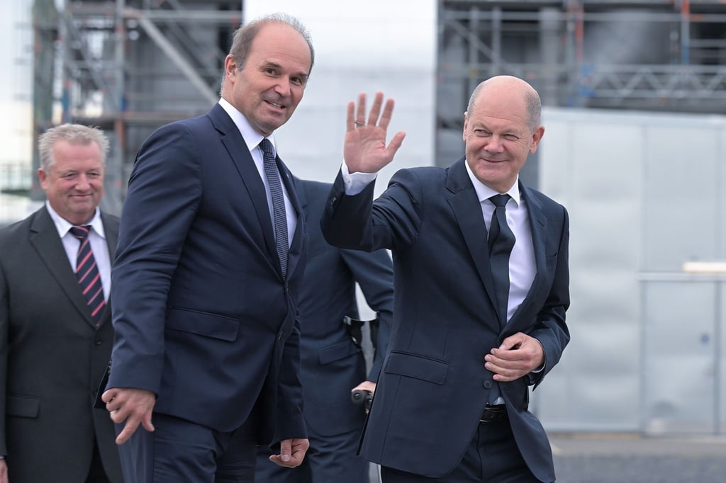 Bundeskanzler Olaf Scholz (SPD, r) geht über das Werksgelände.
