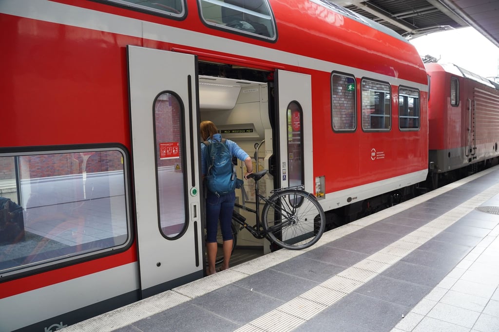 Eine Reisende steigt mit ihrem Fahrrad in eine Regionalbahn Richtung Rostock.