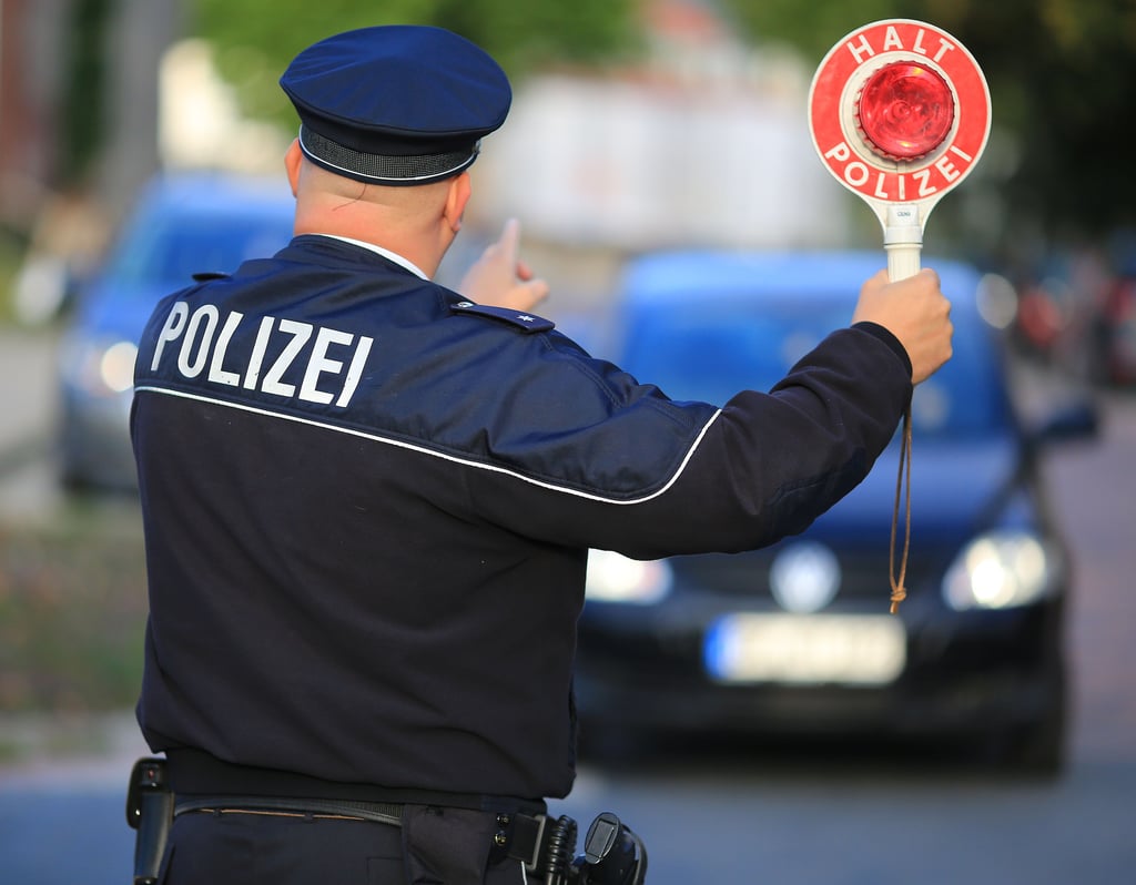Ein Polizist hält einem Autofahrer eine Kelle mit dem Schriftzug «Halt Polizei» entgegen.