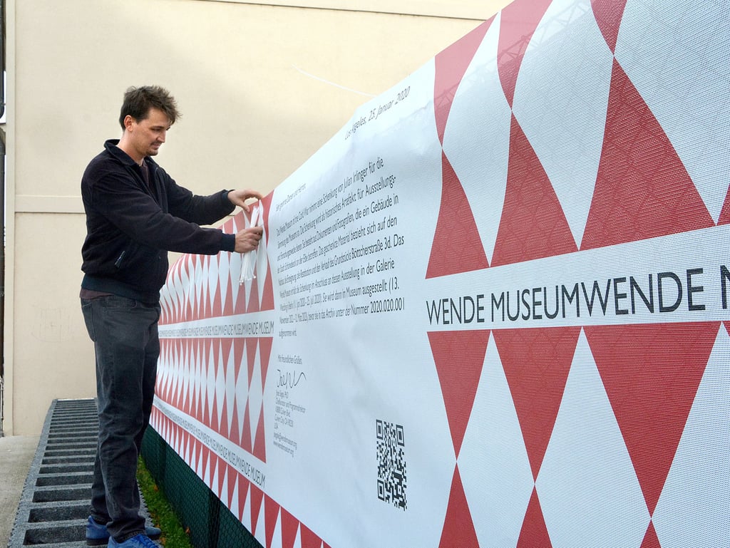 Gregor Peschko ist Kurator des Kunstprojekts „Gift“. Hier befestigt er gerade ein Banner auf dem Marktplatz in Schönebeck. Über aufgedruckten QR-Code können Dokumente und Fotos rund um die Geschichte eines Schönebecker Gebäudes eingesehen werden.